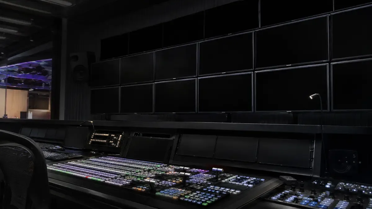 Sala de control con pared de monitores apagados y consola de switcher iluminada