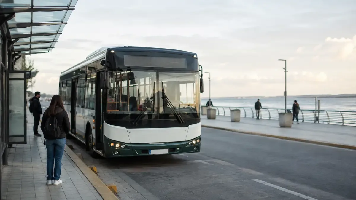 Un colectivo urbano genérico detenido en una parada en un paseo costero junto al río, plano medio documental, perspectiva natural