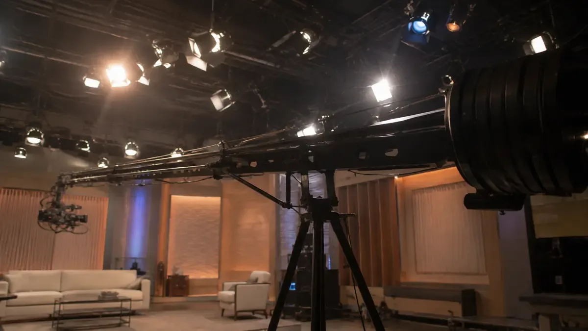 Grua de camara extendida sobre un set vacio con el brazo recortado contra las luces