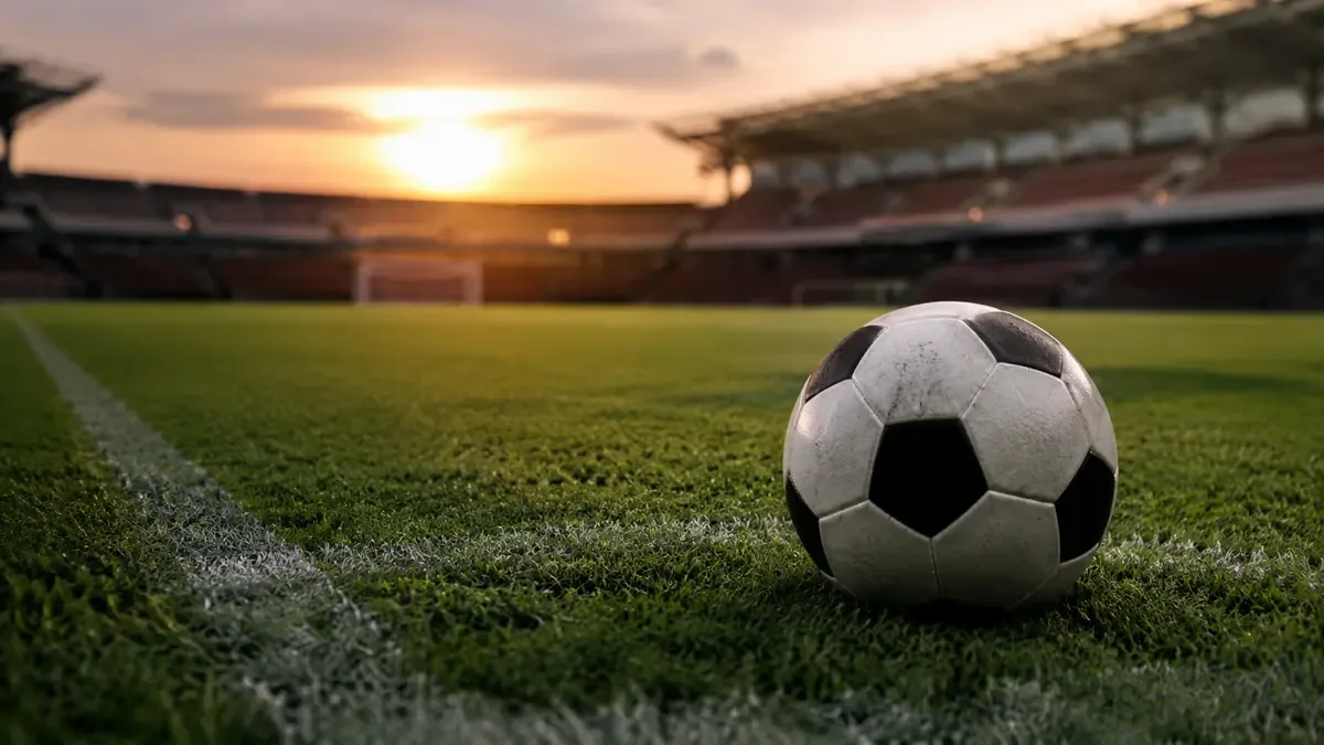 Pelota de futbol apoyada en el cesped de un estadio vacio con las tribunas desenfocadas al atardecer