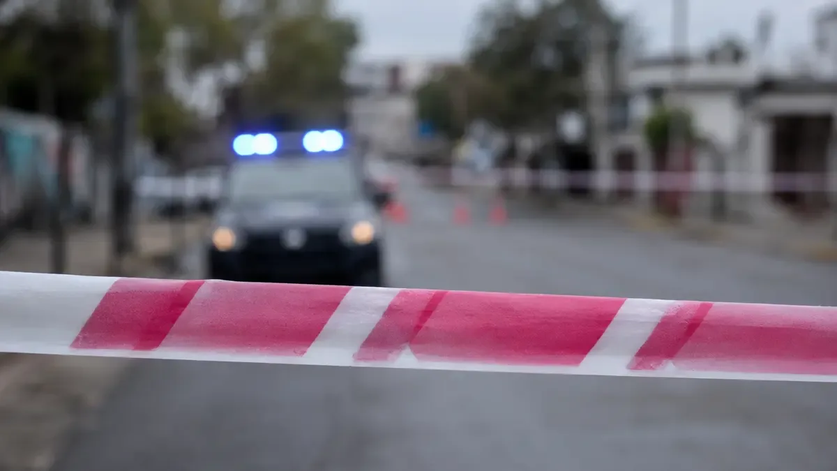 Cinta de vallado policial tensada en primer plano con un patrullero desenfocado al fondo