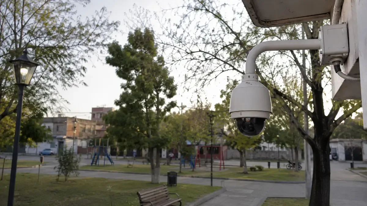 Una cámara de vigilancia genérica en una esquina en una plaza de barrio con mobiliario urbano, plano medio documental, perspectiva natural